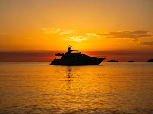 Yacht silhouette on calm water at a vivid golden Bali sunset